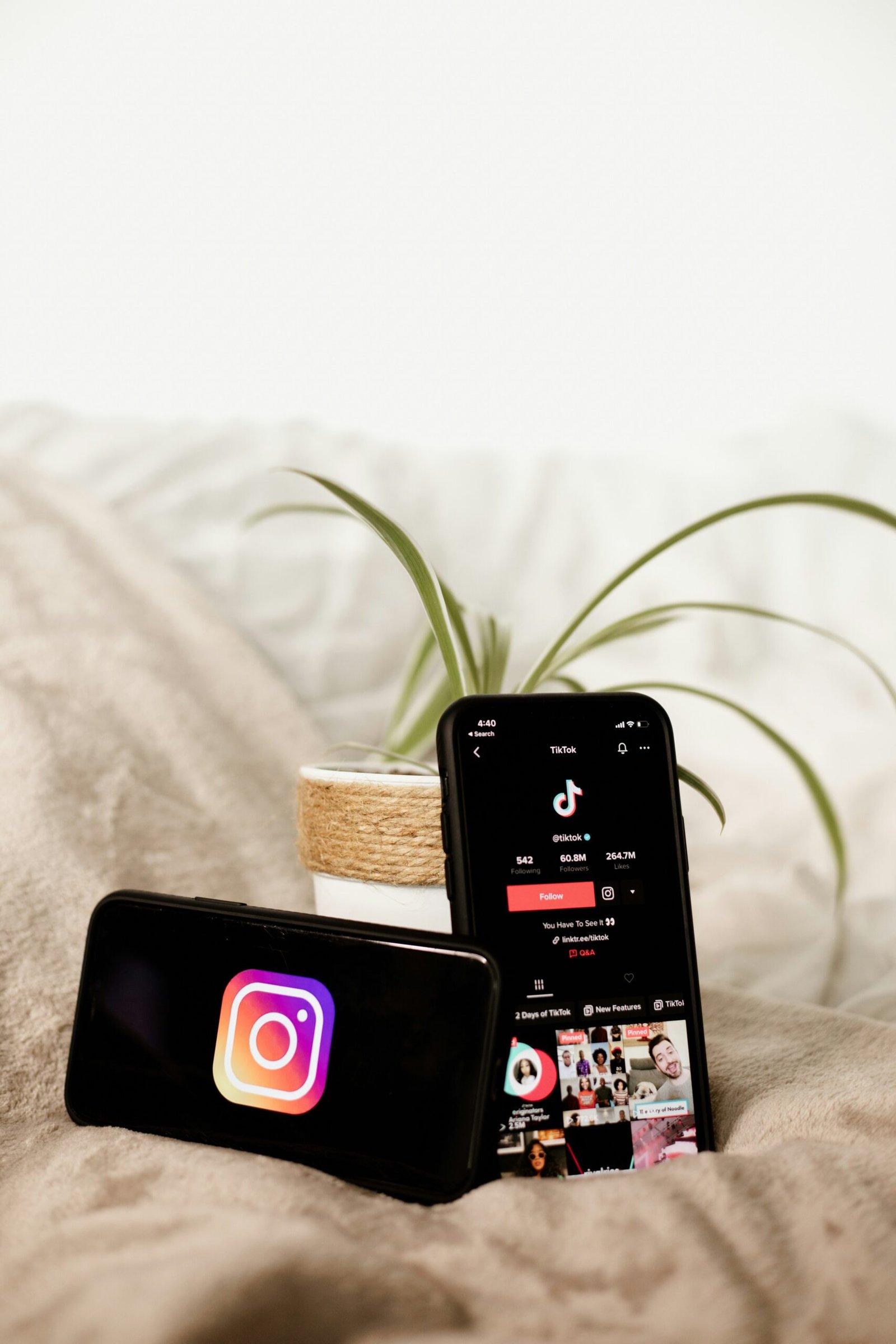 two cell phones sitting on top of a bed next to a plant
